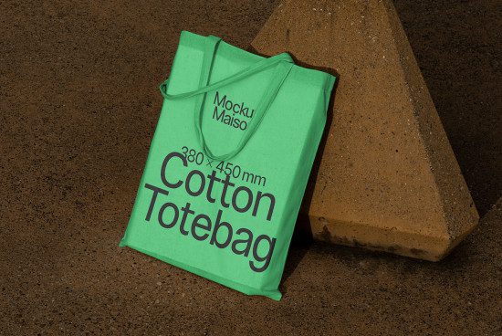 Green cotton tote bag mockup on textured background with concrete block, showcasing custom design space for eco-friendly accessories.