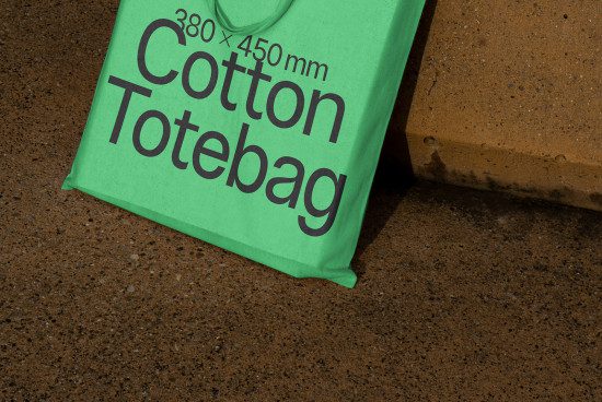 Green cotton tote bag mockup on pavement with dimensions, perfect for eco-friendly bag design presentations for graphic designers.