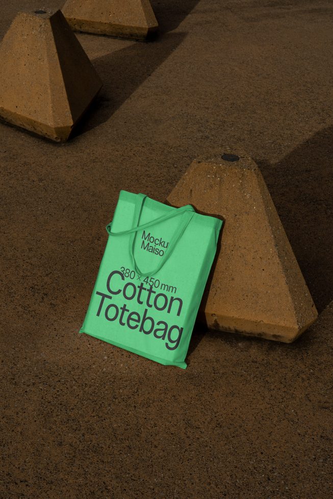 Green tote bag mockup laying on urban concrete with shadows, realistic texture, eco-friendly bag design presentation for marketplace.