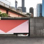 Urban billboard mockup on city street with large blank red and white advertising space for designers to showcase graphics and posters.