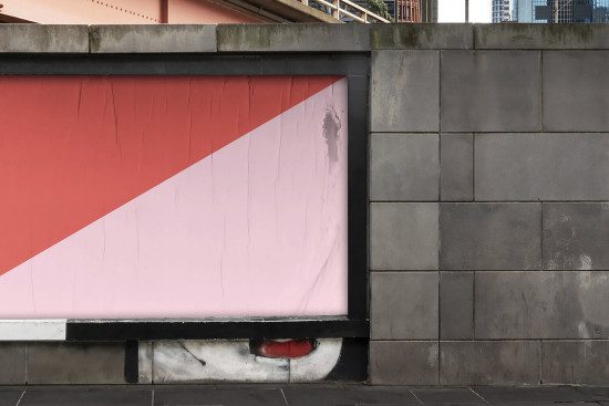 Urban billboard mockup with a geometric split-design in red and pink tones for advertising and design presentations, set against a concrete wall background.