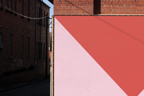 Urban scene with red geometric wall mural for graphic design mockup, showcasing shadows and architectural elements.