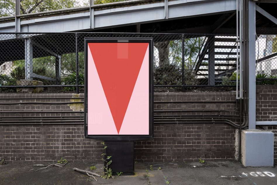 Red V-shape poster on metal stand under industrial overpass structure