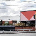Outdoor billboard mockup with a red geometric design template, street view for realistic advertising presentations. Graphic designers' urban mockup asset.