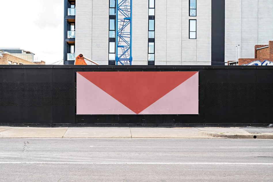 Rectangular hoarding mockup with centered inverted coral triangle on construction barrier