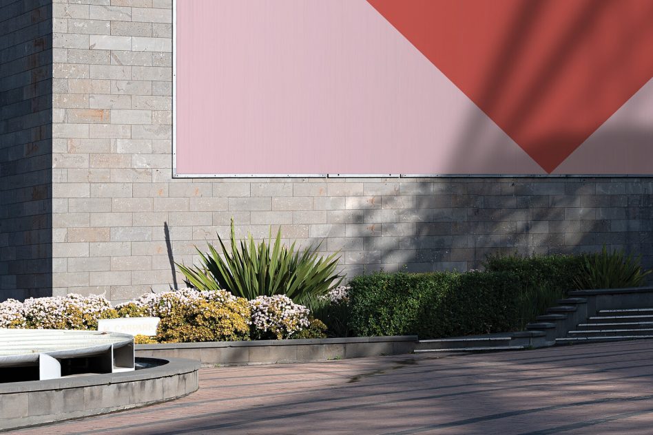 Close-up of tilted geometric poster mockup with coral triangle on modernist stone wall