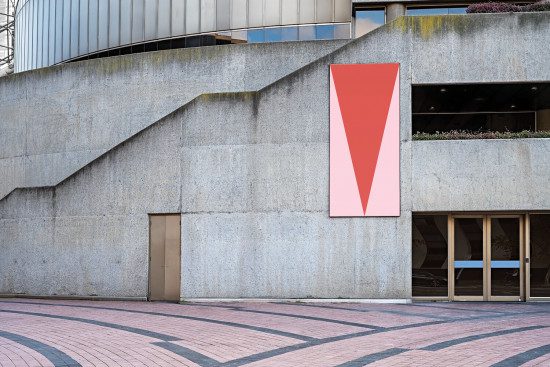 Red geometric poster mockup on an urban building exterior wall with a visible patterned pavement, design presentation, outdoor advertisement.