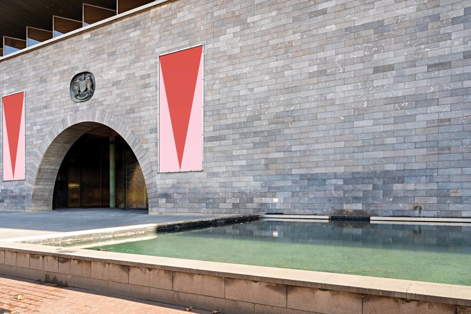 Two vertical posters on historic brick building next to water feature