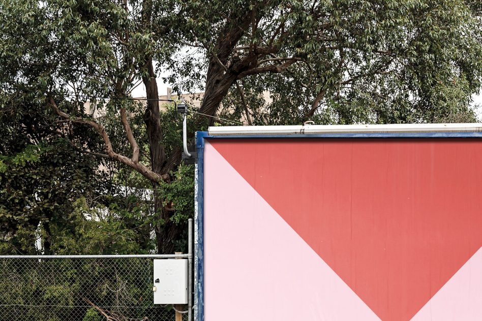 Large outdoor billboard with inverted red triangle on pink, surrounded by leafy trees