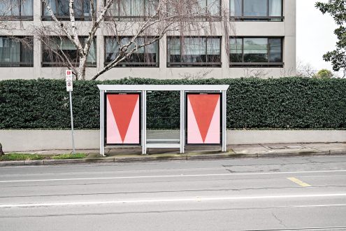 Urban bus stop billboard mockup with minimalist red graphic design poster, street setting with greenery and clear signage.