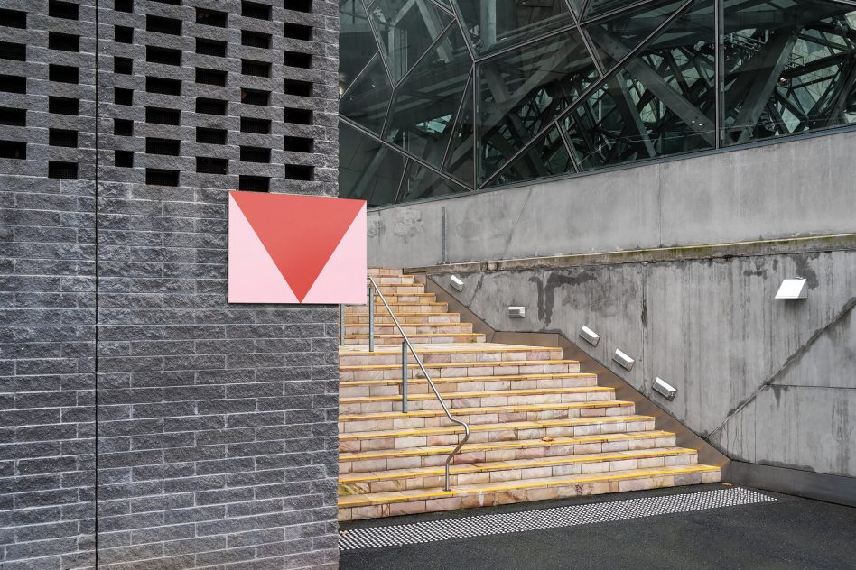 Rectangular sign display on stone building near wooden stairs, glass architecture