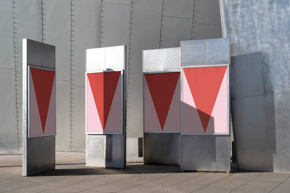 Outdoor advertising mockup of three vertical billboards with red and pink geometric shapes, against a modern gray building wall for design display.