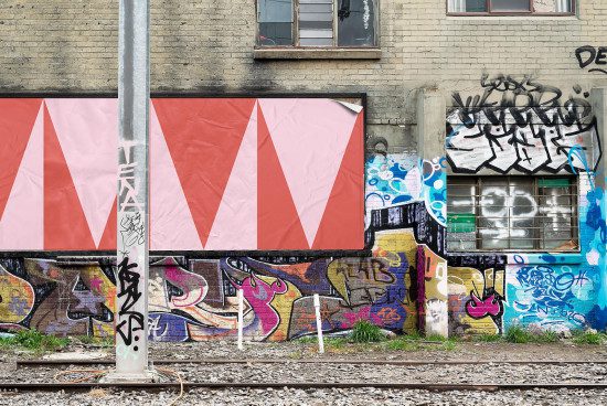 Urban billboard mockup on a graffiti-splashed building beside train tracks, ideal for presenting street-level advertising designs.