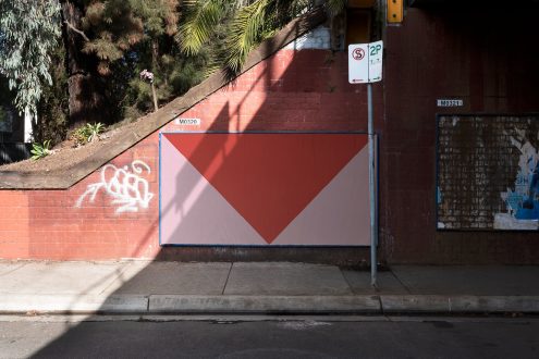 Urban street scene with red brick wall featuring geometric graphic design, possibly useful as a template or mockup background.