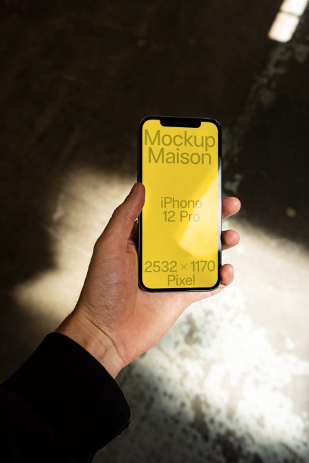 Hand holding iPhone 12 Pro mockup with yellow screen, outdoor light