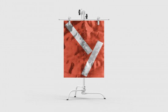 Vertical banner mockup design featuring bold crumpled fabric texture with metallic stripe creating letter V in a minimalist studio setting.