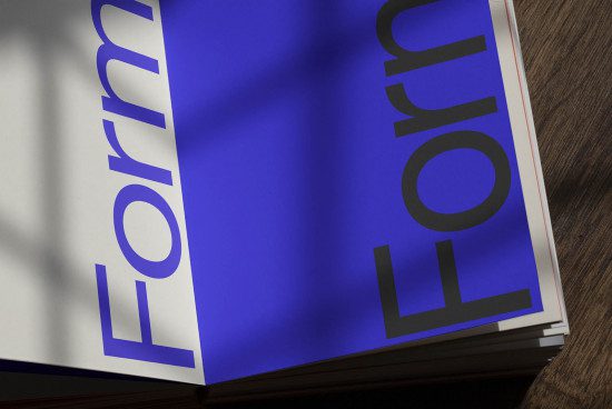 Bold modern font on open magazine mockup with blue overlay, shadow detail, on wooden surface for designer portfolio display.