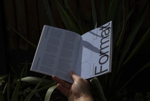 Hand holding an open magazine mockup showcasing font and design layout, with natural background for graphic designers.