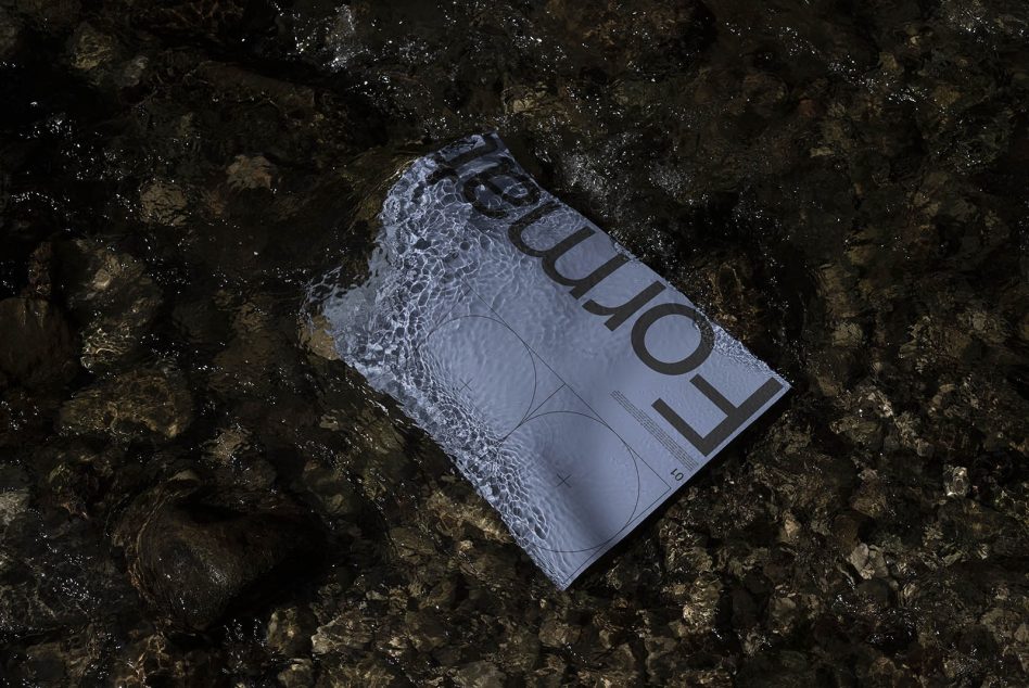Magazine partially submerged in water on mossy rocks with ripple reflections visible