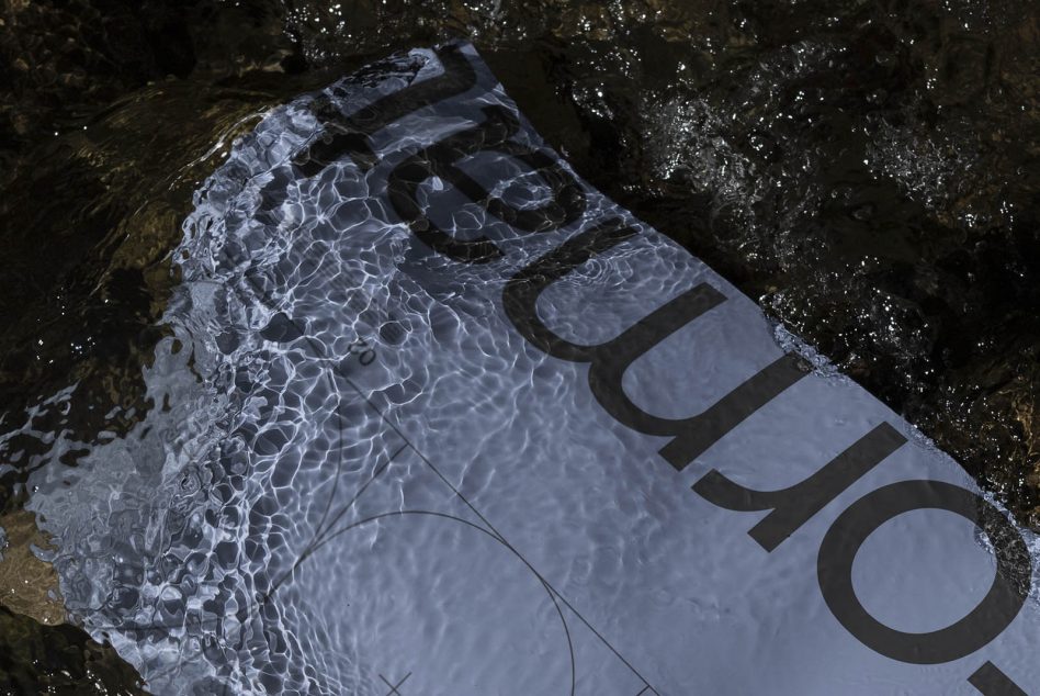 Magazine in shallow water on rocks with wave patterns casting over cover design