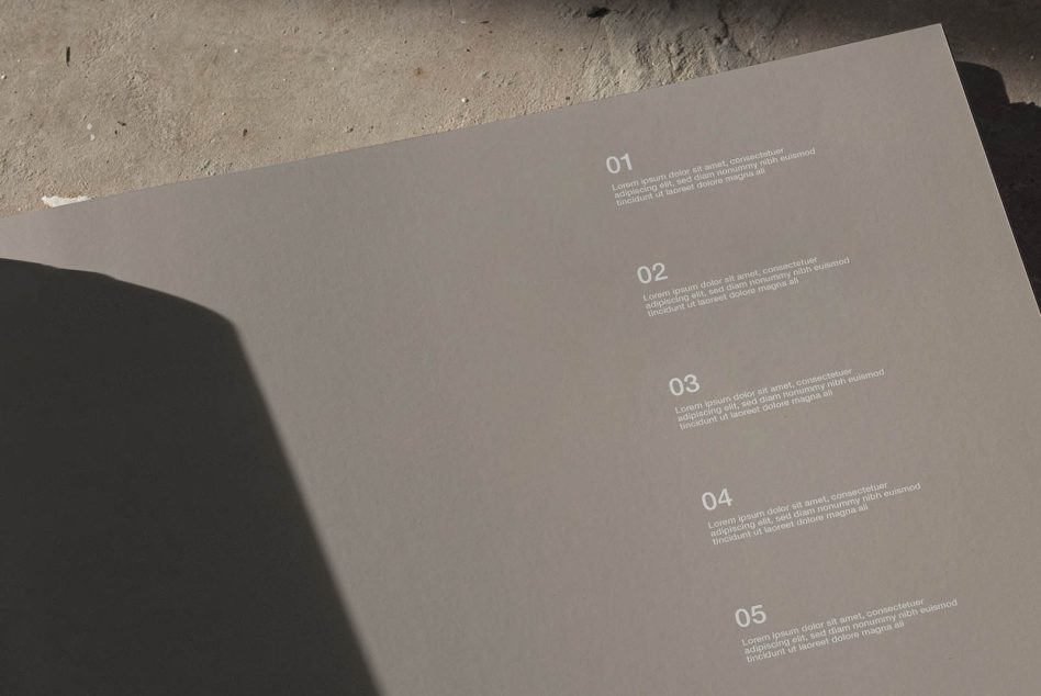 Beige brochure spread with numbered sections 01-05 casting sharp shadows on concrete