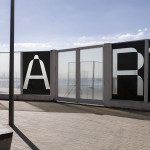 Outdoor urban scene with large "ART" letters on frosted glass panels, sunny day, ideal for graphic design, typography showcase, or mockup.