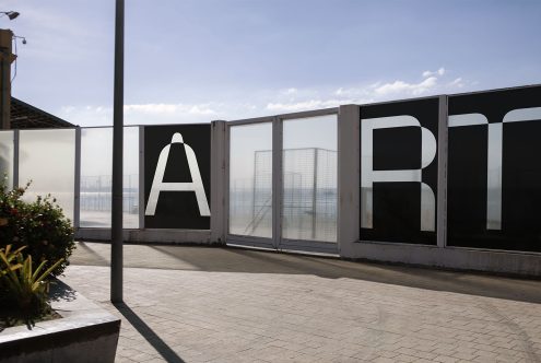 Outdoor urban scene with large "ART" letters on frosted glass panels, sunny day, ideal for graphic design, typography showcase, or mockup.