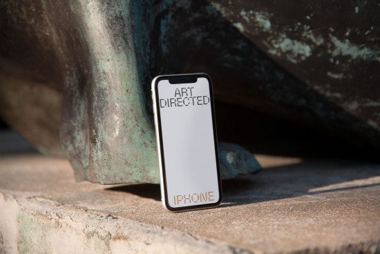 Smartphone mockup on a concrete surface with a textured bronze sculpture in the background, perfect for app design presentation.