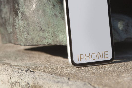 Smartphone mockup template leaning against rustic metal texture, blank screen for design, clear daylight setting, realistic shadows.