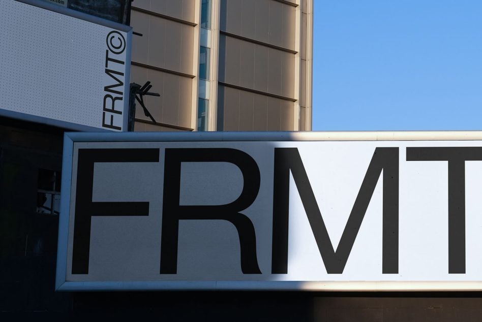 FRMVT text on modern storefront sign with glass tower building reflected behind