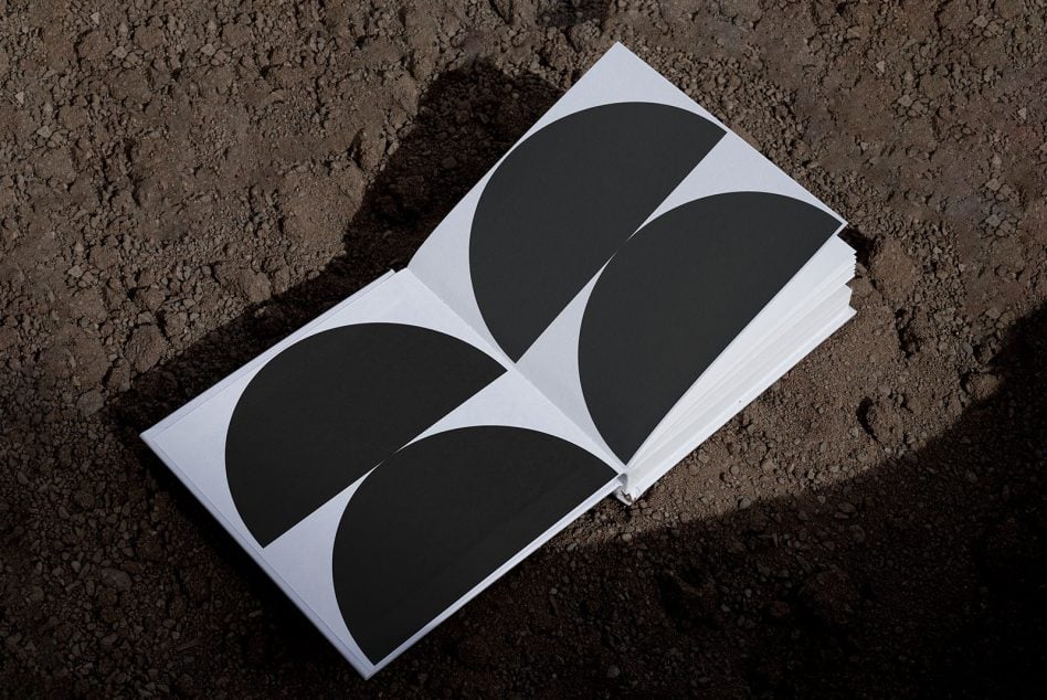 Magazine opened to show four black circular half shapes arranged across spread on dirt