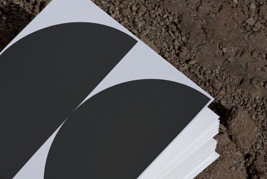 Stack of blank black and white paper mockups on a textured ground surface, ideal for branding presentations and design showcases.