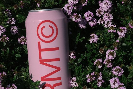 Pink beverage can mockup with modern graphic design, nestled in a bed of purple flowers for eco-friendly packaging concepts.