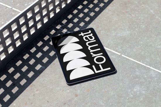 Tablet mockup laying on concrete ground displaying design sample with reflective screen, urban setting, digital assets, realistic shadows.