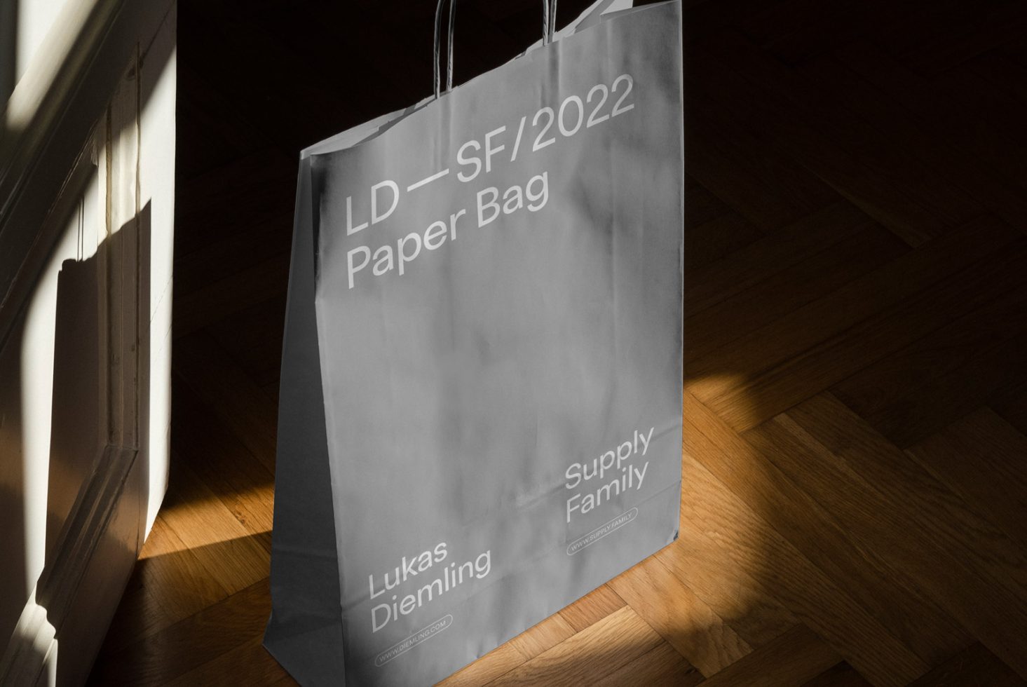 Elegant paper bag mockup on wooden floor with natural light, showcasing typography and branding potential for designers.