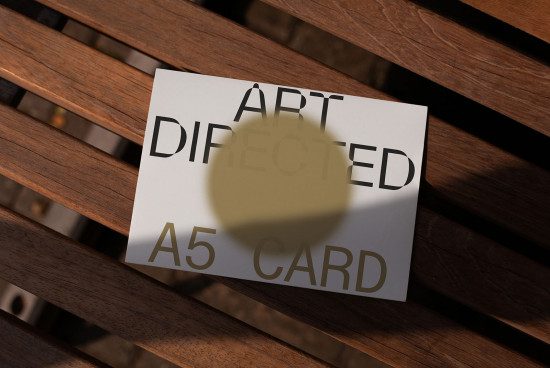 Printed A5 card mockup on wooden bench with typography, realistic shadows, outdoor lighting, design presentation, editable template.