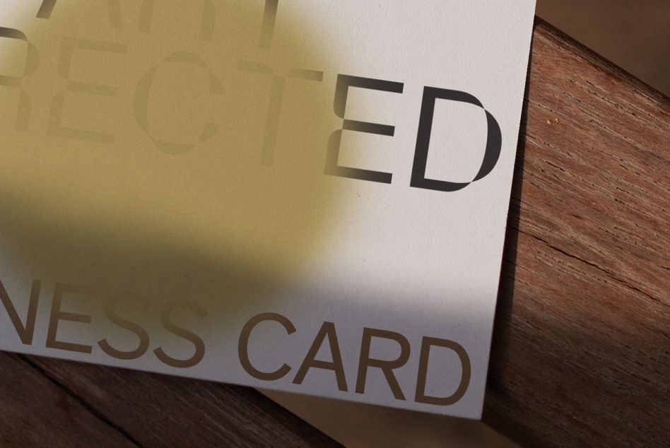 Business card mockup on wood surface with gold foil stamped text casting shadows