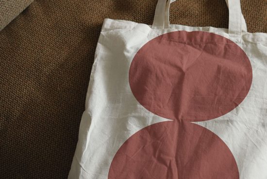 White tote bag mockup with red circular graphic design lying on a textured brown fabric, ideal for presentations and showcasing designs.