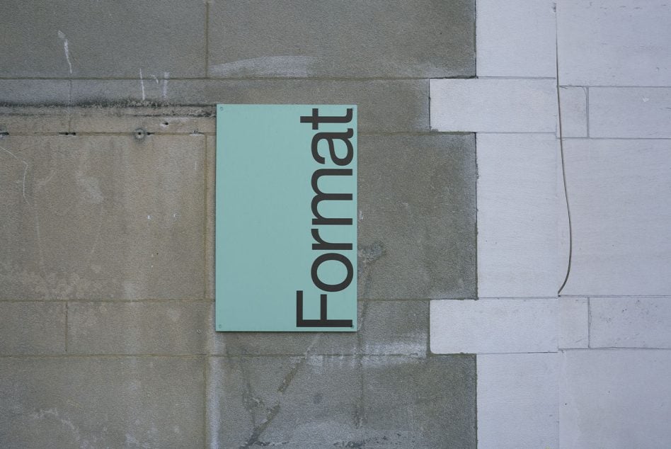 Mint green rectangular sign on stone blocks with black vertical lettering Format