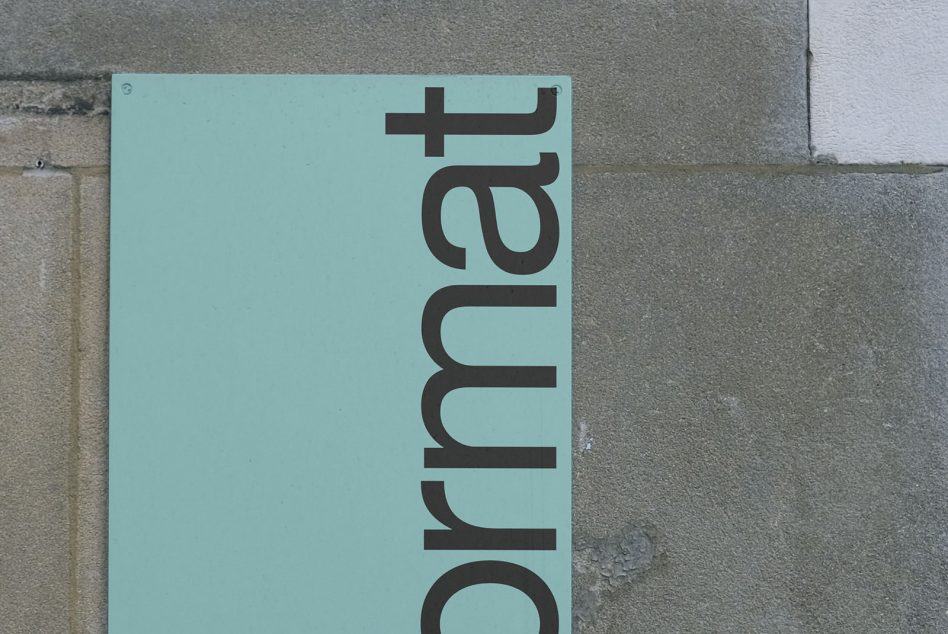 Turquoise square plaque mounted on concrete wall with black vertical text Ohmart