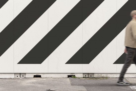 Man walking by a wall with bold diagonal black and white stripes, ideal for urban mockup or graphic design backdrop.