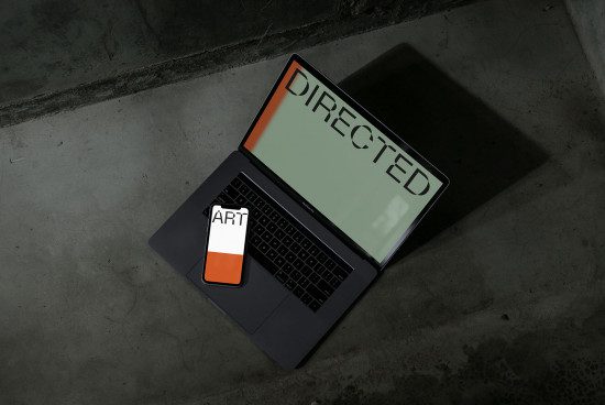 Laptop mockup on concrete floor with creative directed screen design and art themed phone, ideal for designer presentations.