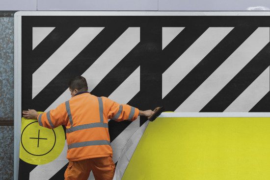 Worker applying adhesive black and white graphic design decal on wall, high-visibility clothing, design mockup in urban setting.