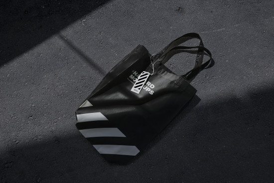 Black tote bag mockup on asphalt with label tag, realistic shadows, for branding presentation, graphic design assets for marketplace.