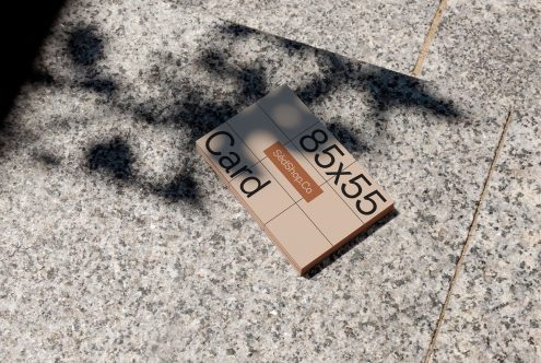 Business card mockup laying on textured sidewalk in sunlight creating shadows, ideal for presenting designs to clients.