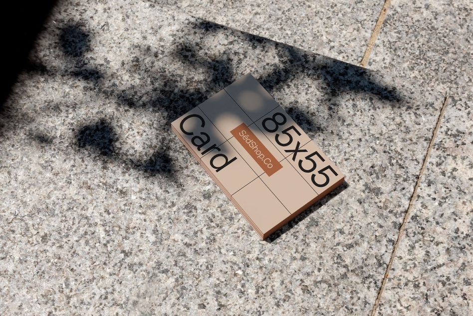 Business card mockup laying on textured sidewalk in sunlight creating shadows, ideal for presenting designs to clients.