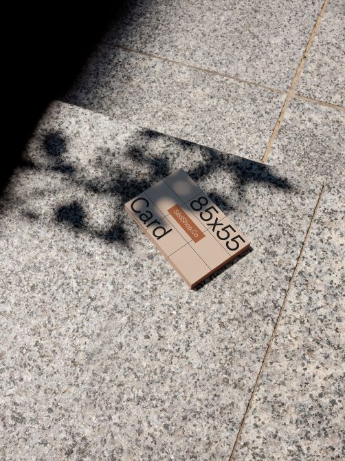 Business card mockup on textured stone pavement in sunlight with natural shadows for realistic design presentation, ideal for graphic designers.