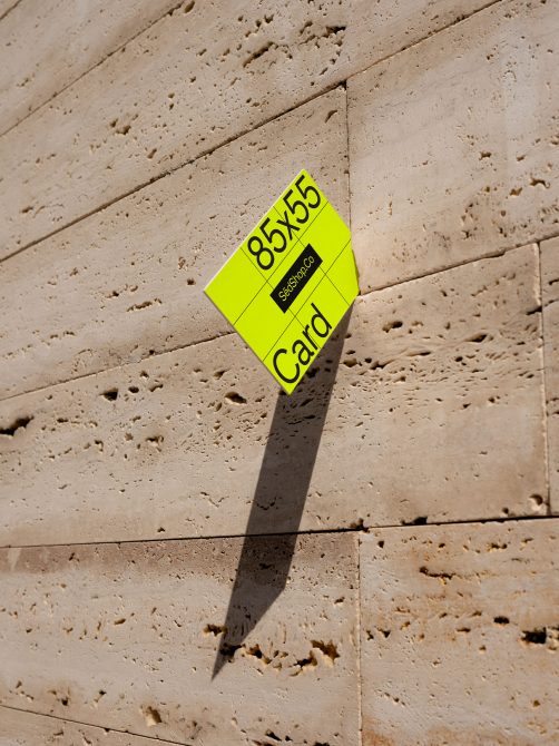 Neon yellow 85x55 business card mockup casting shadow on textured travertine wall