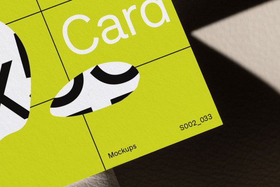 Close-up view of a vibrant yellow business card mockup with black and white abstract design elements, highlighted by natural shadows.