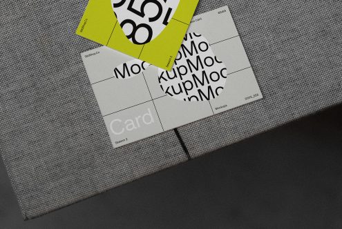 Business card mockup with modern design elements scattered on a textured grey fabric surface, providing a realistic presentation for branding.